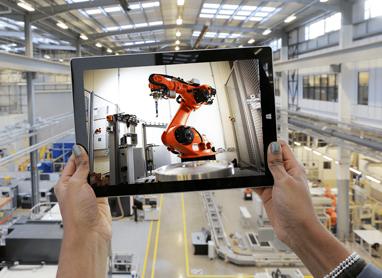 Hands holding up a tablet showing manufacturing equipment